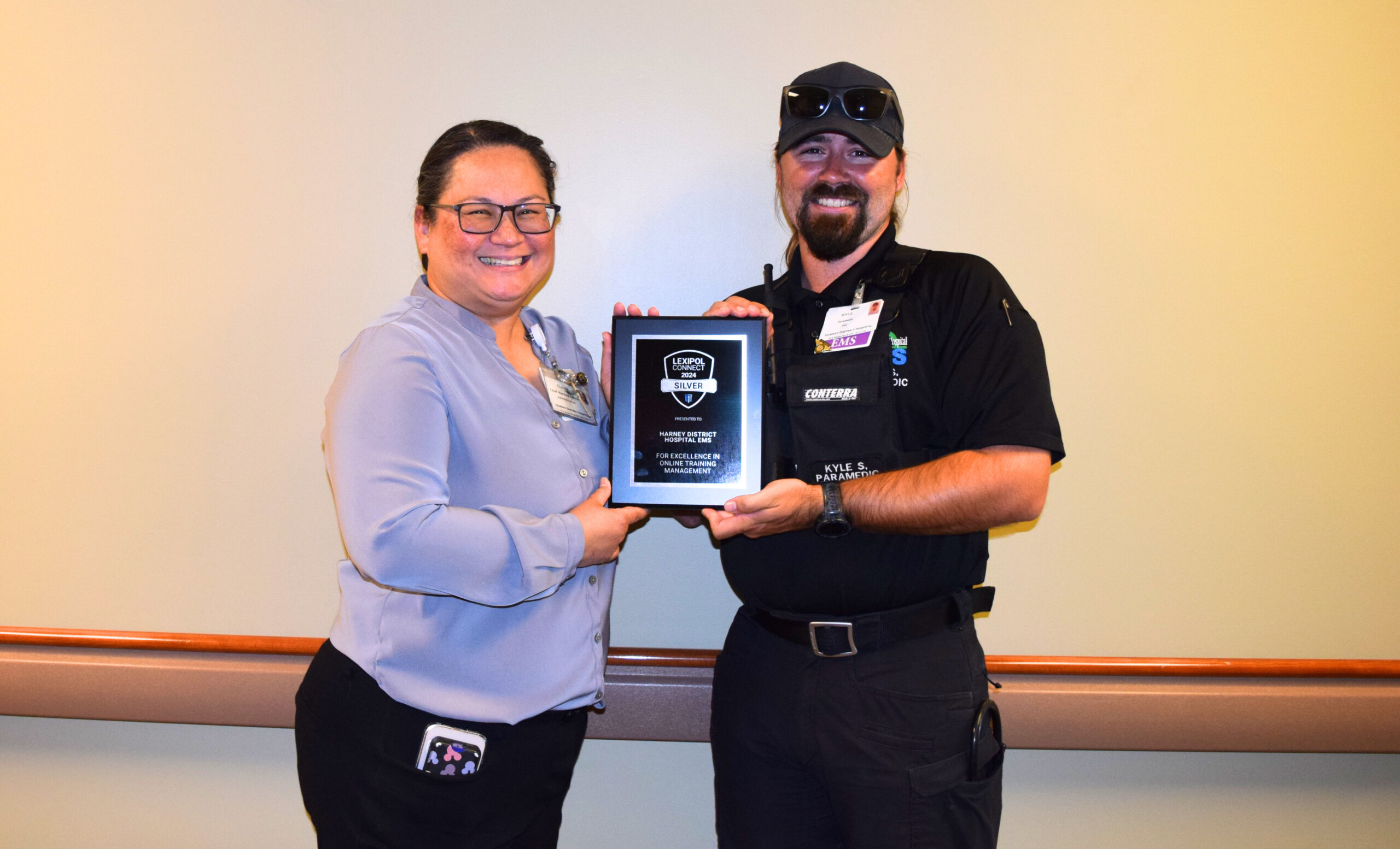 Chief Nursing Officer Elaine Wulff handing a plaque to Emergency Medical Services Manager Kyle Snider. The plaque says, "Lexipol Connect 2024 Silver presented to Harney District Hospital EMS for excellence in online training management."